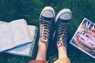 Two sneakered feet sit in the green summer grass surrounded by open books