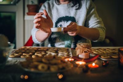 A person in a sweater dusts a sheet of cookies with sugar.