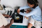 young girl sitting on counter cracking an egg into a pan