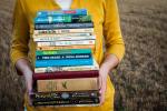 Person in yellow cardigan holds a stack of fiction books