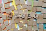 Over some rainbow colored stripes are a bunch of blank scrabble tiles with five tiles spelling out the word "Pride".