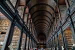 A long corridor lined with marble busts with a high curved ceiling and dark wood with shelves of books branching off from either side of it.